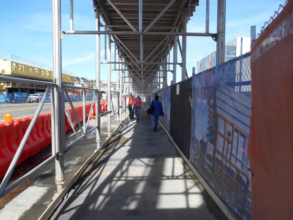 a sidewalk with scaffolding above.