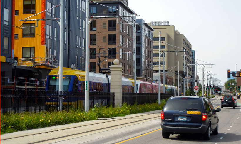 A car going traveling down a road next to tall buildings.